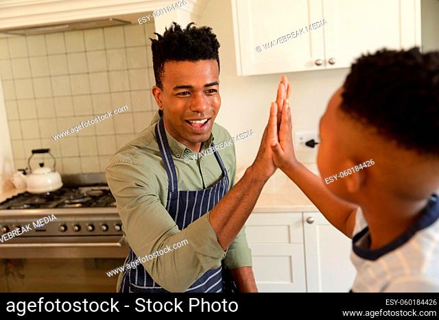 Happy african american father and son high fiving in kitchen before cooking