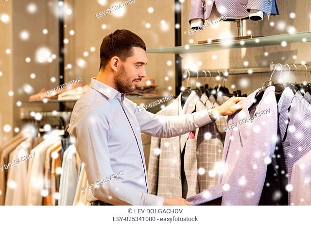 sale, shopping, fashion, style and people concept - elegant young man in shirt choosing clothes in mall or clothing store over snow