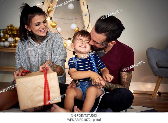 Happy boy opening Christmas present with his parents at home