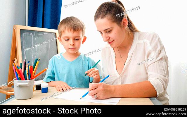 Teacher teaching drawing her little toddler son with colorful pencils at school classroom. Concept of parenting and education at home