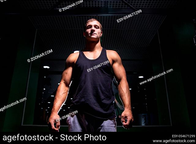 Portrait of young muscular sportsman looking at camera in gym.From below