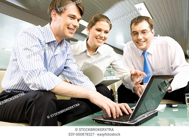 Portrait of young businesswoman holding documents and pointing at the monitor of laptop surrounded by two men