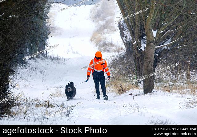 06 December 2023, Mecklenburg-Western Pomerania, Qualitz: A man walks his dog along a snow-covered path during snowfall. Persistent snowfall and temperatures...