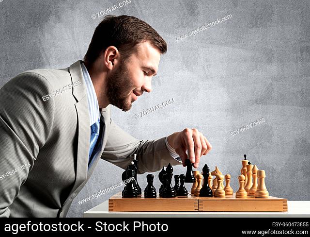 Concentrated businessman playing chess game. Successful management and leadership concept. Confident young man in business suit sitting at desk with chess