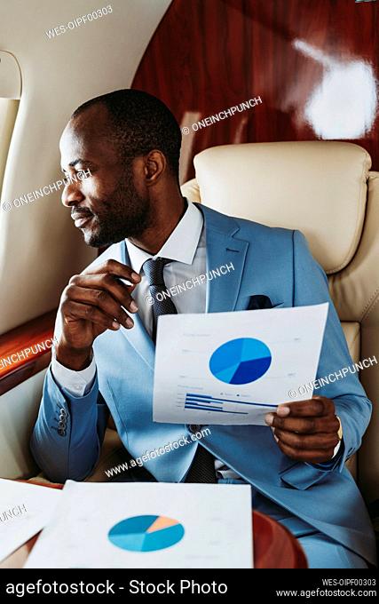 Businessman with pie chart looking through window in airplane