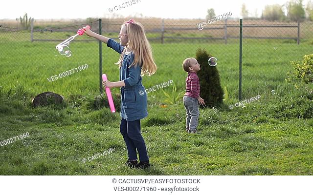 Joyful siblings playing with soap bubbles outdoors