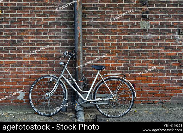 Rotterdam, Netherlands. Idle Bike parked agaisnt a rainpipe and old, industrial wall, waiting for it's onwner to collect it for her commute