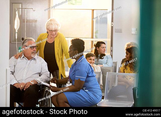 Female nurse talking with senior patient in wheelchair in clinic lobby