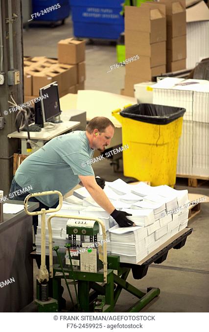 worker with ear protection in a printing plant, handling a load of paper on a pallet. NR