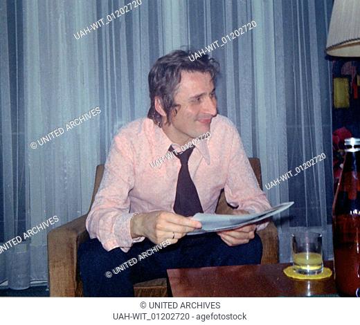 Ein junger Mann sitzt bei Freunden im Wohnzimmer bei einem Drink in den 1970er Jahren