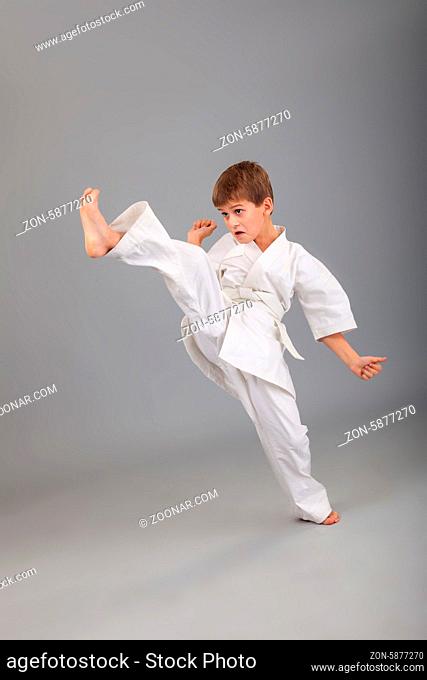 Karate boy in white kimono fighting isolated on gray background