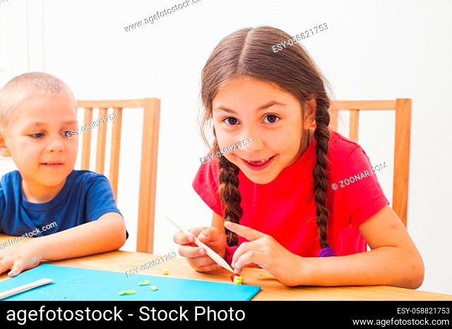 Brother and sister having fun together with colorful modeling clay at at home. Children play with plasticine or dough