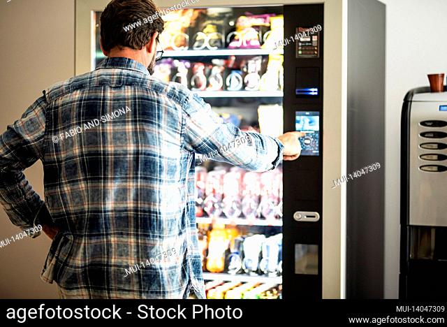 back view of adult mature man choosing snacks and drinks on 24h free automated distributor - people buying food on airport gate - travel lifestyle and junk...