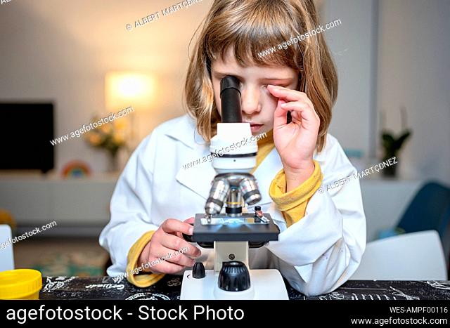 Girl in lab coat looking through microscope at home
