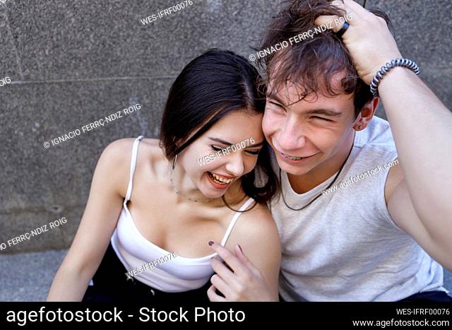 Cheerful young couple sitting against wall
