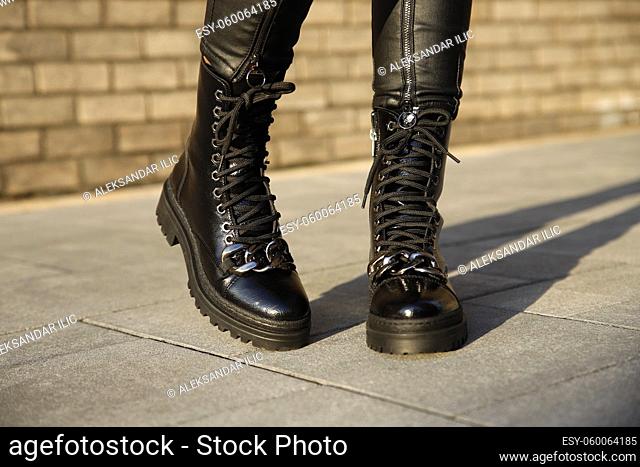 Woman in stylish leather black boots and jeans outdoors. Close up of female legs in fashion footwear