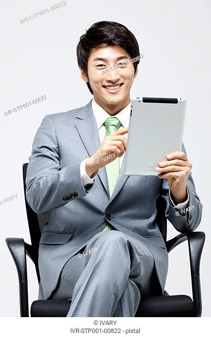 Asian Businessman Sitting On Chair With Leg Crossed Holding Digital Tablet In Hand