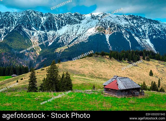 Amazing alpine countryside place with rickety wooden hut and high snowy Piatra Craiului mountains, Pestera village, Transylvania, Romania, Europe