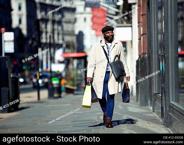 Businessman with shopping bags walking on sunny city sidewalk