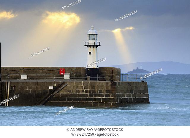 Shafts of light behind the lighthouse on Smeaton's Pier at St Ives in Cornwall, with Godrevy Island and lighthouse in the distance