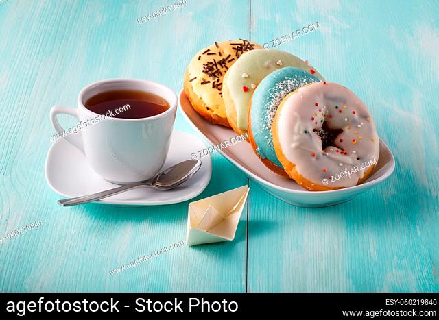 Four donuts on old wood table with cup of tea and origami