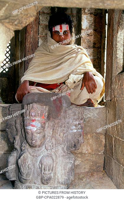 Nepal: A young Sadhu (Holy Man) sits above a four-faced Shivalingam, Pashupatinath, Kathmandu