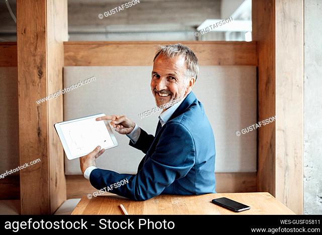 Smiling businessman showing business plan on digital tablet in office