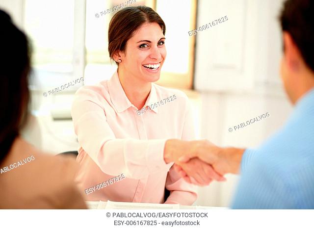 Female bank manager giving a hand greeting to executive man while smiling and sitting on workplace