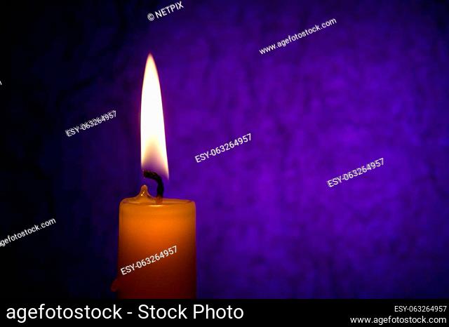 Single yellow wax candle burning alone in the dark blue background. Conceptual image symbolize peace, love, hope or patience with free copy space