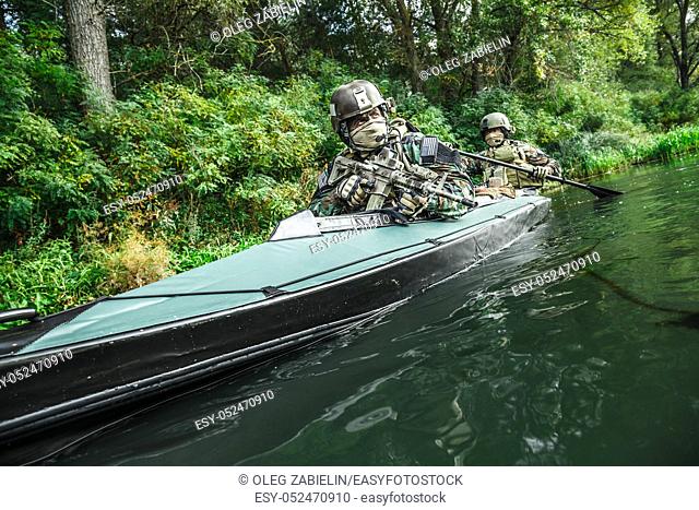 Special forces men with painted faces in camouflage uniforms paddling army kayak. Boat moving across the river, diversionary mission, diagonal view