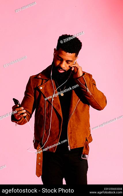 Stylish, handsome and cool African American man with beard, listening to music, texting, isolated on pink studio background