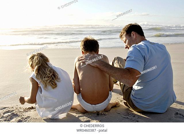 Rear view of a mid adult man with his two children on the beach