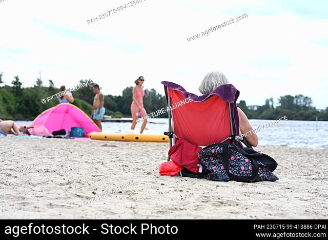 15 July 2023, Timmel: A woman sits in a deck chair at a bathing lake reading a book. Weekend vacationers and tourists have sought cooling on the coasts and...