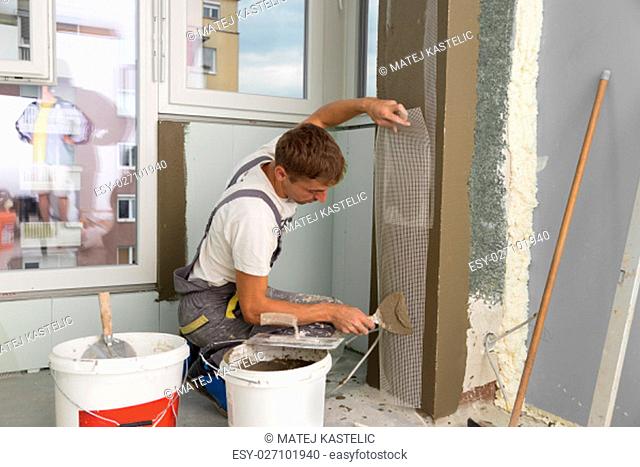 Construction worker wearing worker overall with wall plastering tools renovating apartment house. Plasterer renovating indoor walls and ceilings with float and...