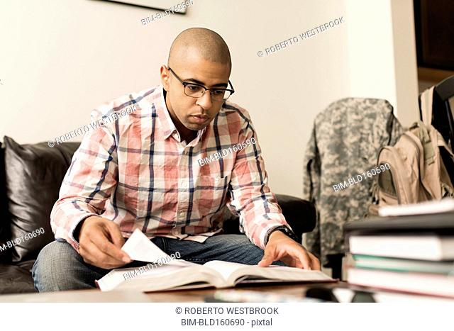 Mixed race soldier reading book on living room sofa