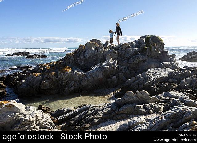 Two children, a teenage girl and eight year old boy exploring the jagged rocks and rockpools on a beach