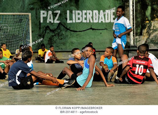 Teenagers and children on a playground, wall with lettering Paz Liberdade, Portuguese for Peace Freedom at the back, Favela Morro da Formiga slum