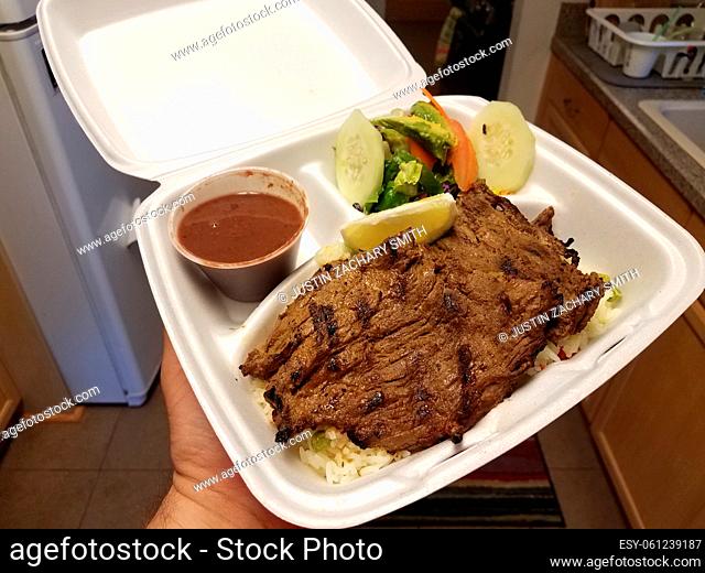 grilled steak and salad and beans and rice in take out container in kitchen