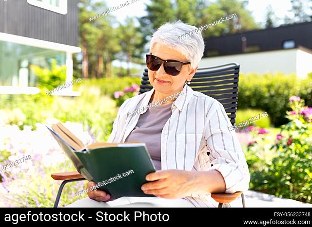 happy senior woman reading book at summer garden