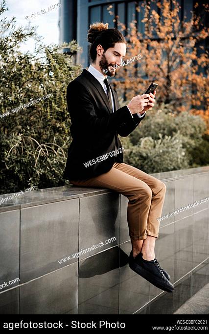 Businessman using mobile phone while sitting on retaining wall