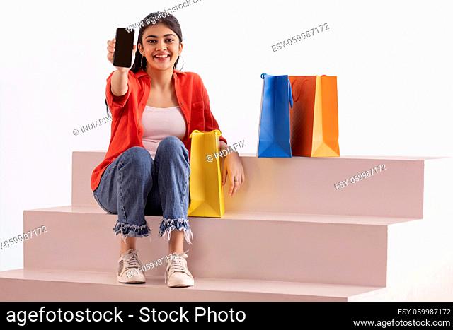 A woman sitting with colorful carrybags on stairs showing mobile phone
