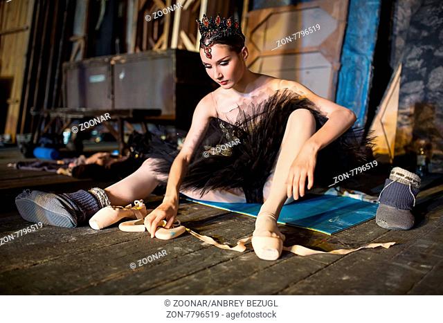 Prima ballerina sitting on the warm-up backstage before going on stage for a solo program on the stage in a performance of Swan Lake, view the profile