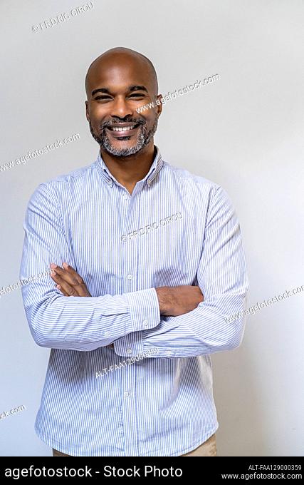 Smiling man standing with arms crossed against white wall
