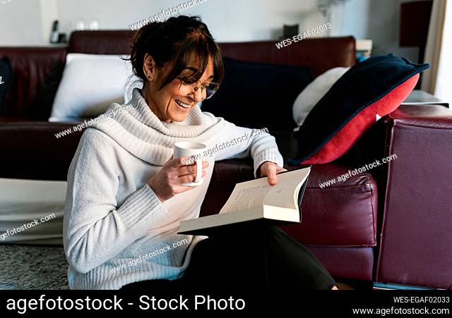 Woman with coffee cup smiling while reading book at home