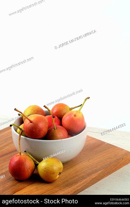 White bowl with small pears on wooden board