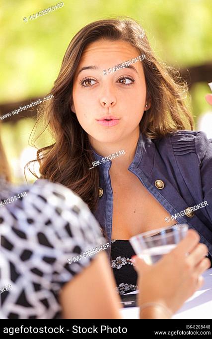 Expressive young adult woman having drinks and talking with her friend outdoors