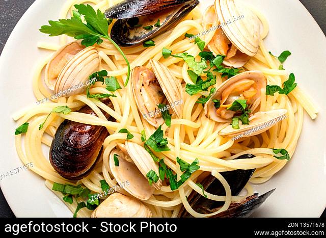Close-up of spaghetti vongole, Italian seafood pasta with clams and mussels, in plate with herbs on rustic stone background