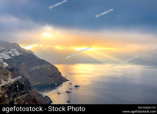 Greece. Heavy clouds over the caldera of Santorini. Sun Rays illuminates the bay and several anchored yachts