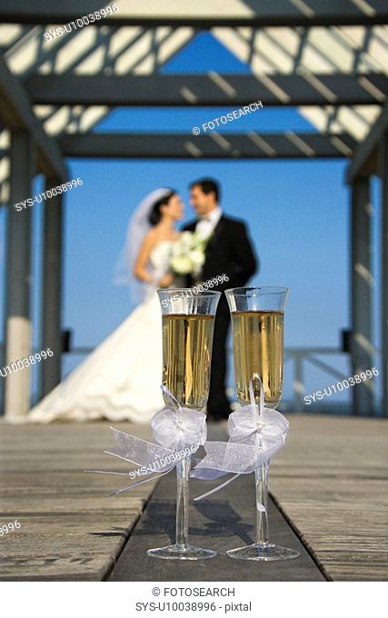 Pair of flute glasses of champagne with Caucasian bride and groom blurred in background