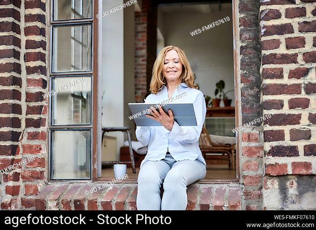Happy businesswoman using tablet PC sitting on doorway